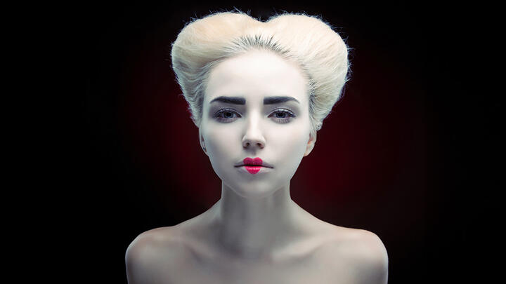 A young woman painted white with a red heart on her lips and a hairstyle reminiscent of England's Queen Elizabeth I